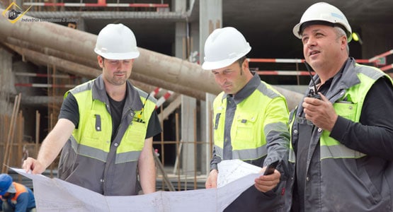 three construction or contract workers with hard hats and vests on looking at plans